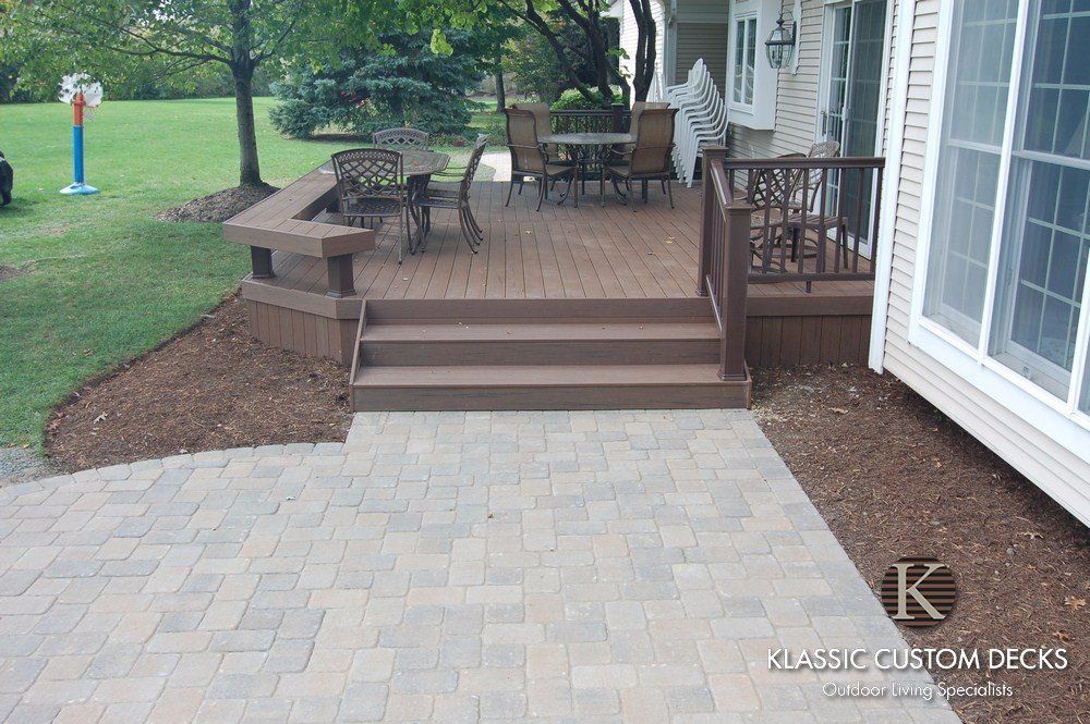 Wooden backyard deck with steps, patio furniture, and a brick paver patio beside a house
