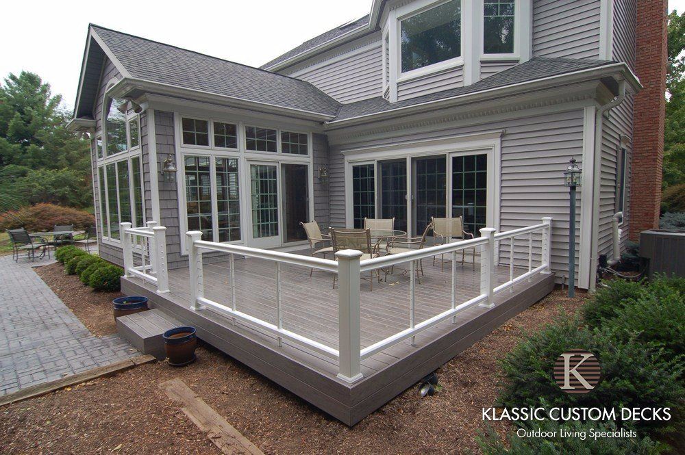 White composite deck with railing attached to a gray house, viewed from the backyard