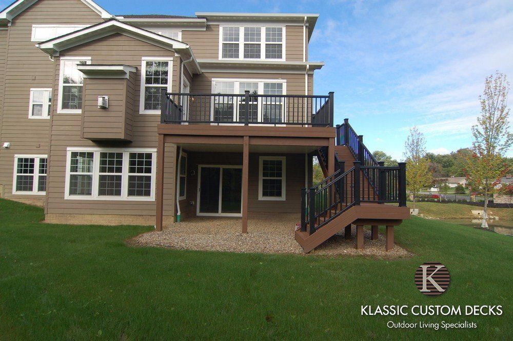 Back deck and staircase on a beige house with black railings and a grassy yard