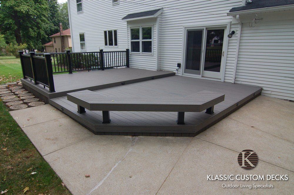 Raised composite deck with black railings and a low ramp beside a white house