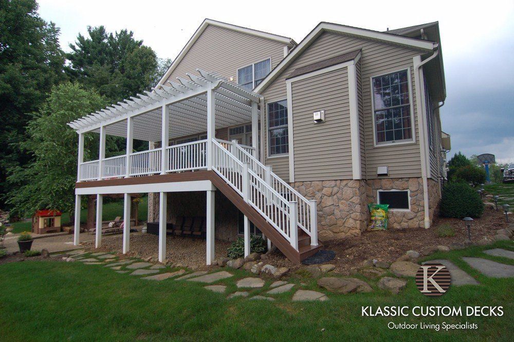 White screened porch and elevated wooden deck with stairs on a house, with stone foundation and green yard.