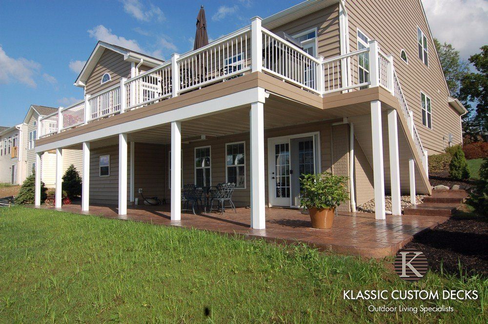 Two-story tan house with white trim and a raised deck over a grassy lawn