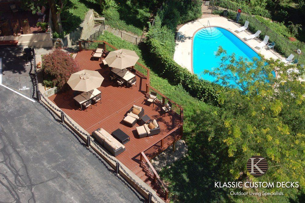 Wood deck patio with beige umbrellas and lounge chairs beside a turquoise pool and trees
