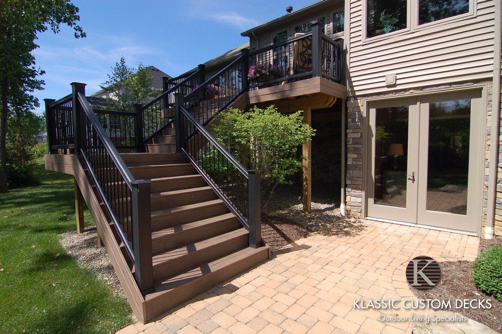 Wooden deck stairs leading to an elevated backyard deck beside a house, with patio below.