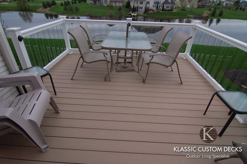 Backyard deck with glass patio table and four chairs, wooden railing, and white lattice skirting