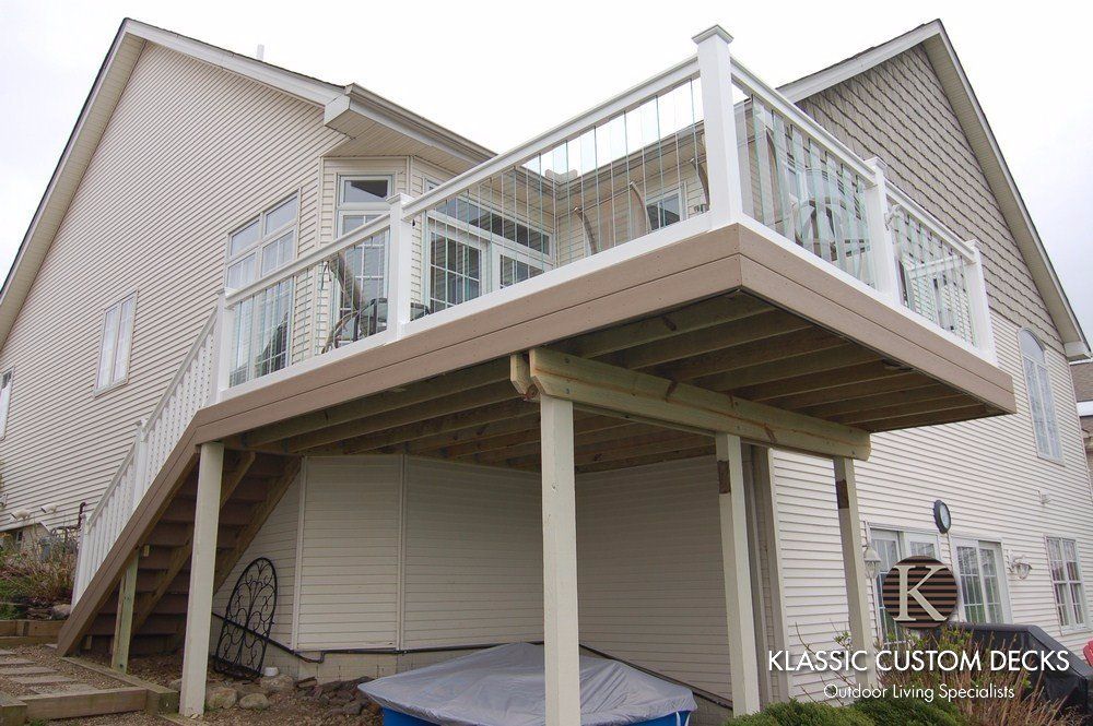 Raised wooden deck attached to a beige house with white railings and stairs over a covered patio