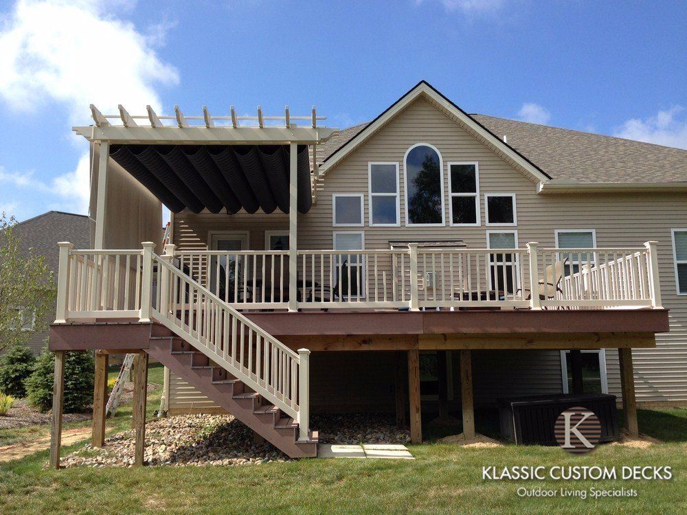 Elevated beige house with large wooden deck, stairs, and covered patio under a blue sky
