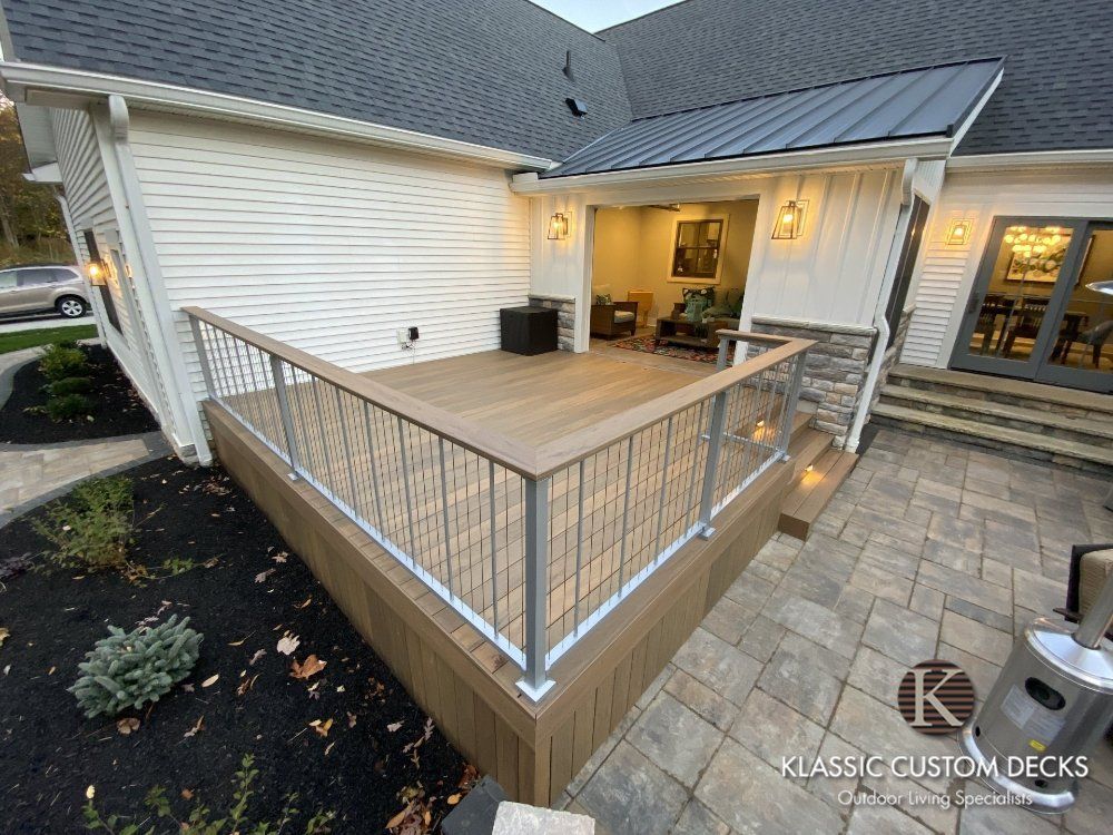 Wooden deck with metal railing beside a house patio, overlooking a landscaped yard at dusk