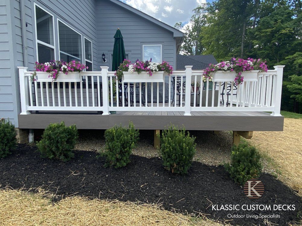 White deck with flower boxes on a gray house, supported by posts over a mulch bed.