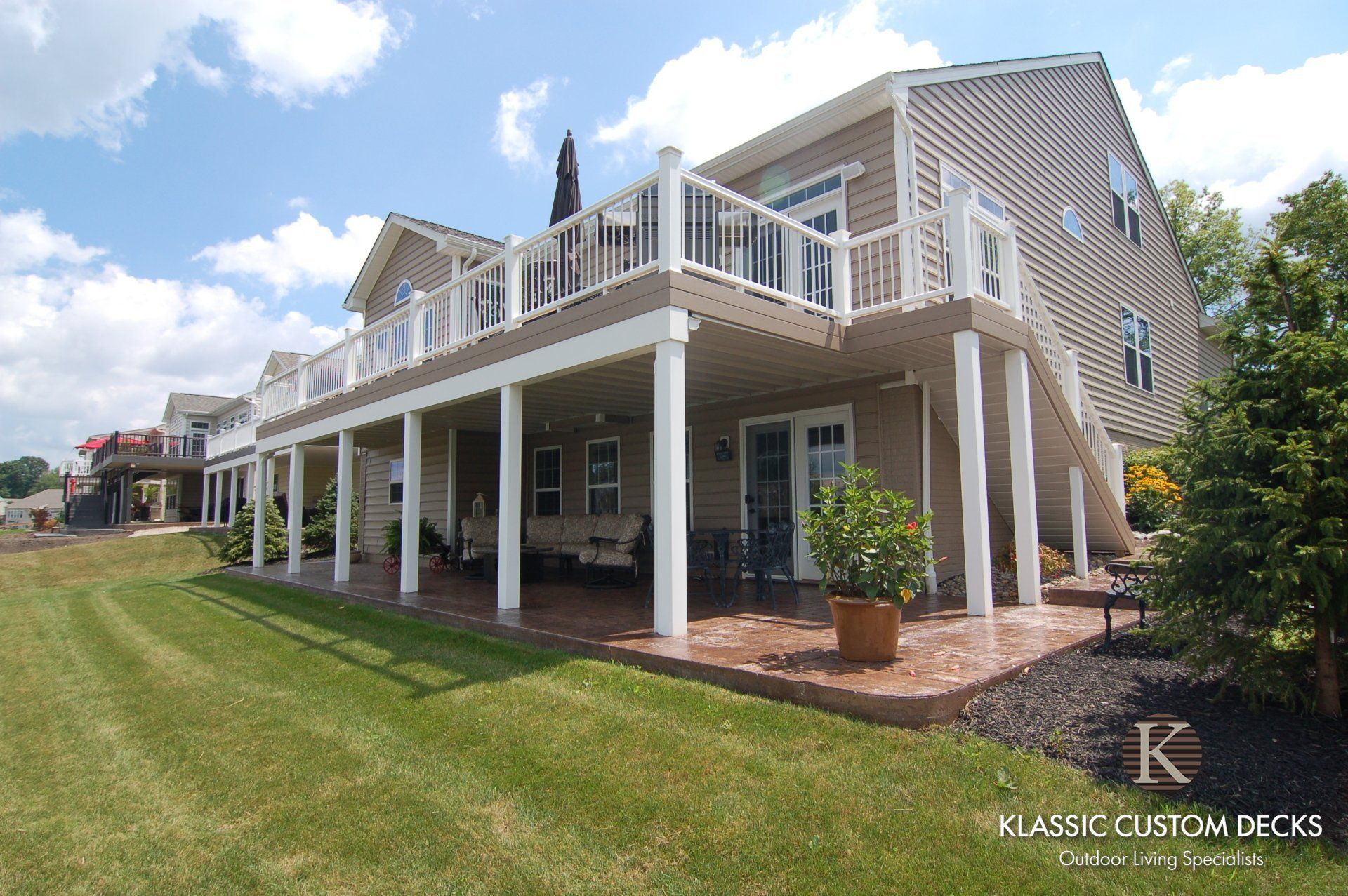 Raised beach house with white deck and columns beside a grassy lawn under a blue sky