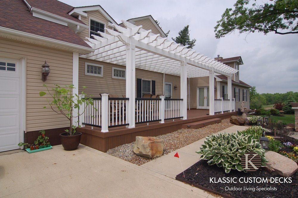 Back patio with white pergola, wood deck, brick house exterior, and landscaped garden border