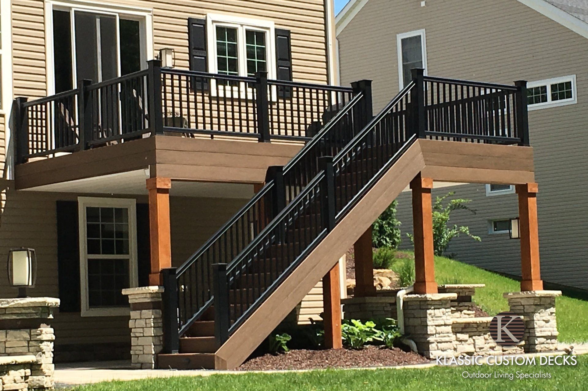 Back deck with black railings and stairs on a beige house with stone columns and a lawn below