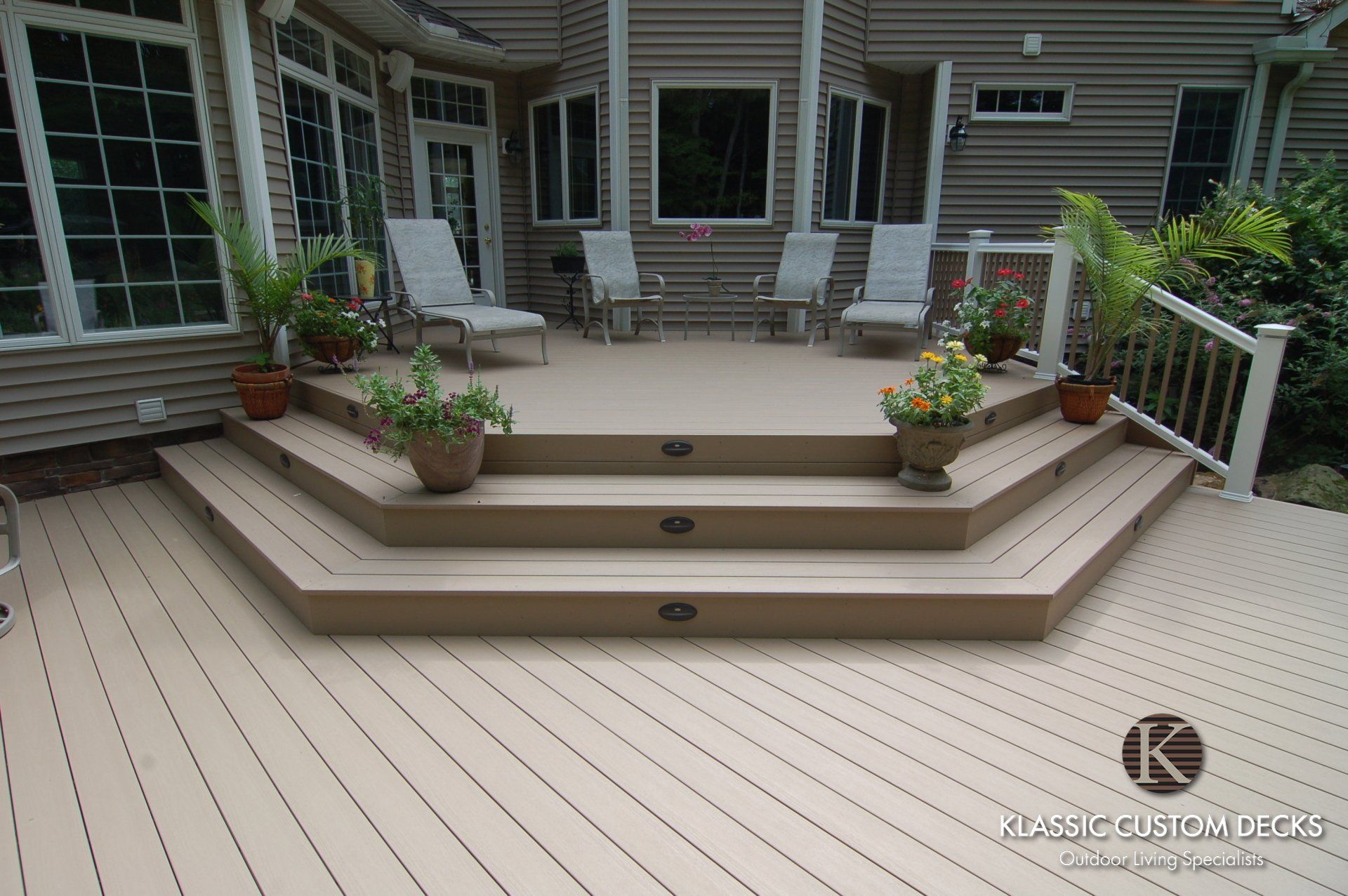 Multi-level backyard deck with steps, potted plants, and white railing outside a gray house