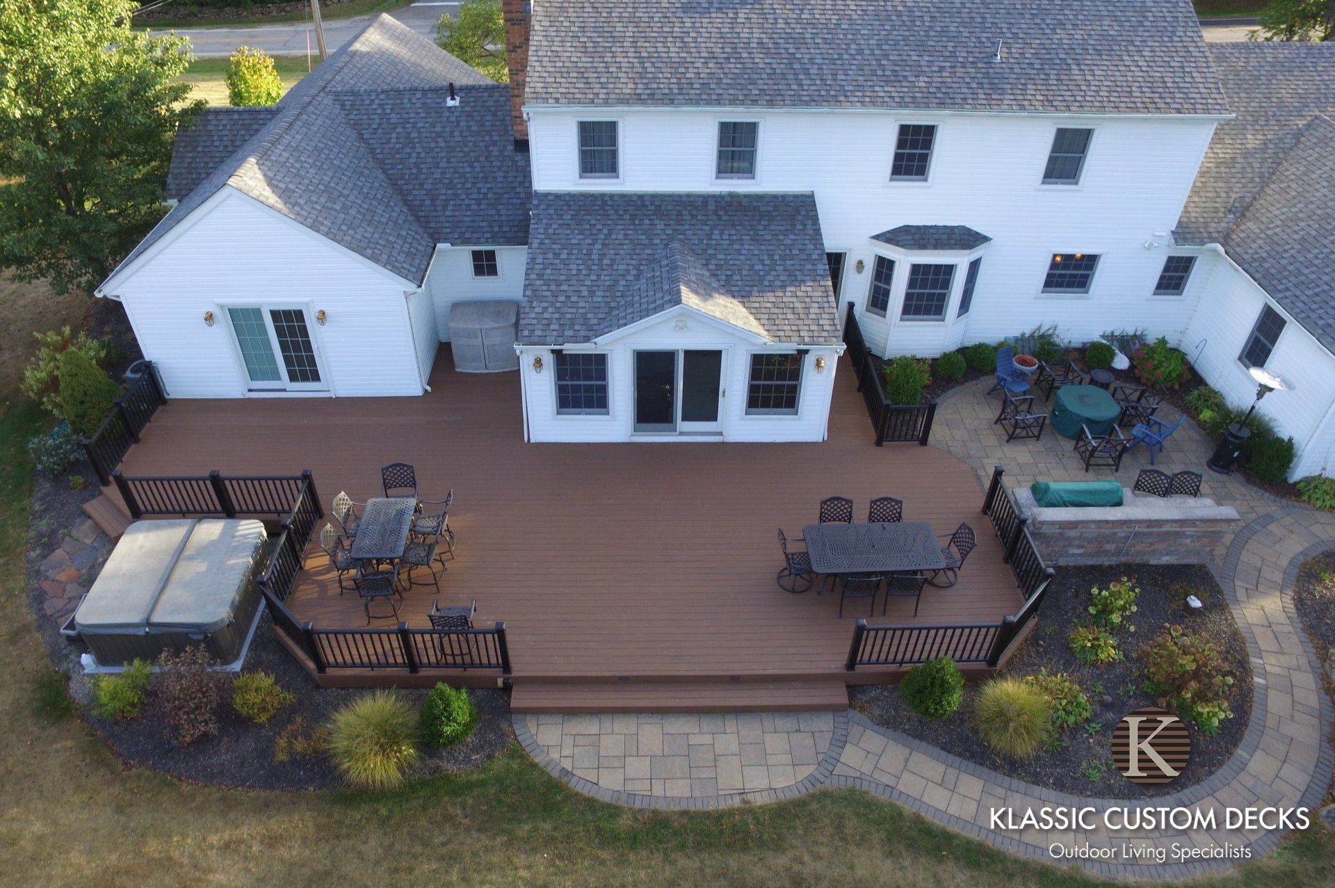 Aerial view of a white house with a large wooden deck, patio furniture, and landscaped backyard