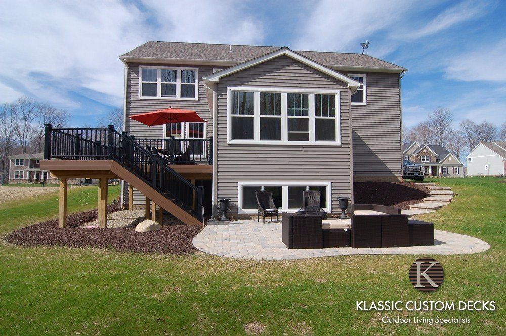 Backyard house with a raised wooden deck, stairs, and patio furniture on a grassy lawn.