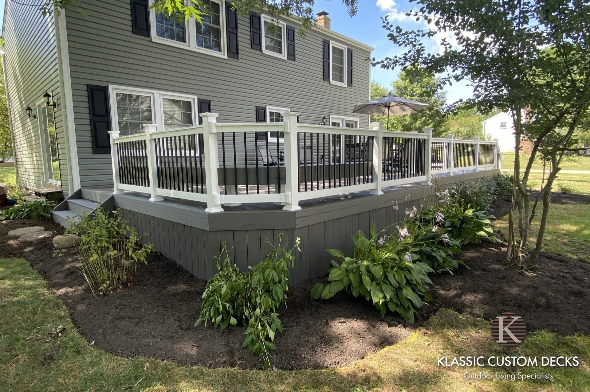 Gray house with a white-railed wooden deck and stairs in a landscaped yard