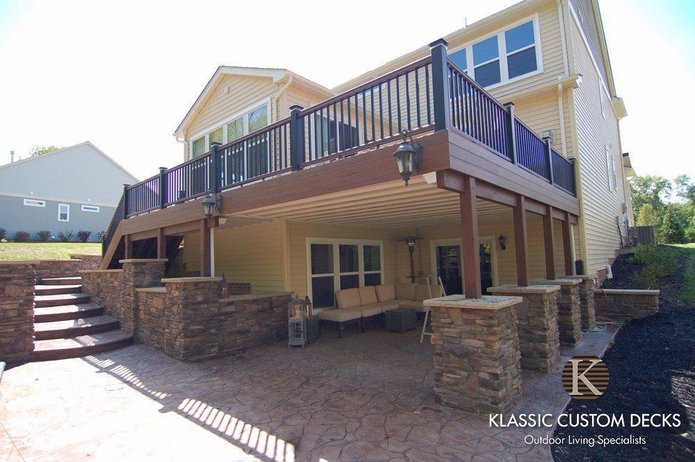 Large raised wooden deck with black railings on a house, stone support walls, and stairs on the left.