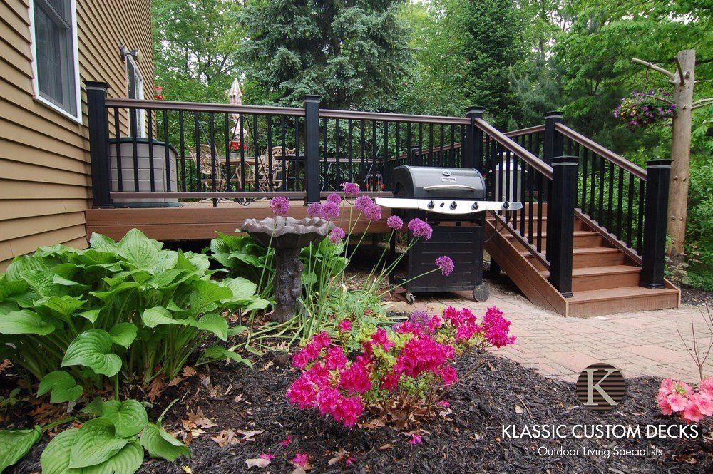 Backyard deck with black railings, hot tub, and pink flowers beside a brown house