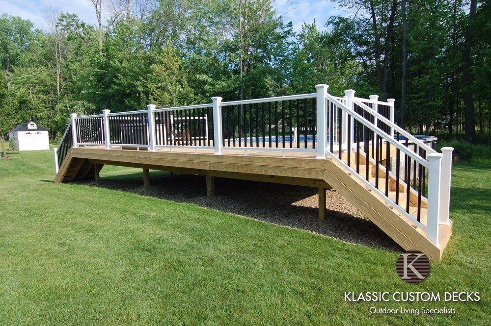 Raised wooden deck with white railings and stairs in a grassy backyard area