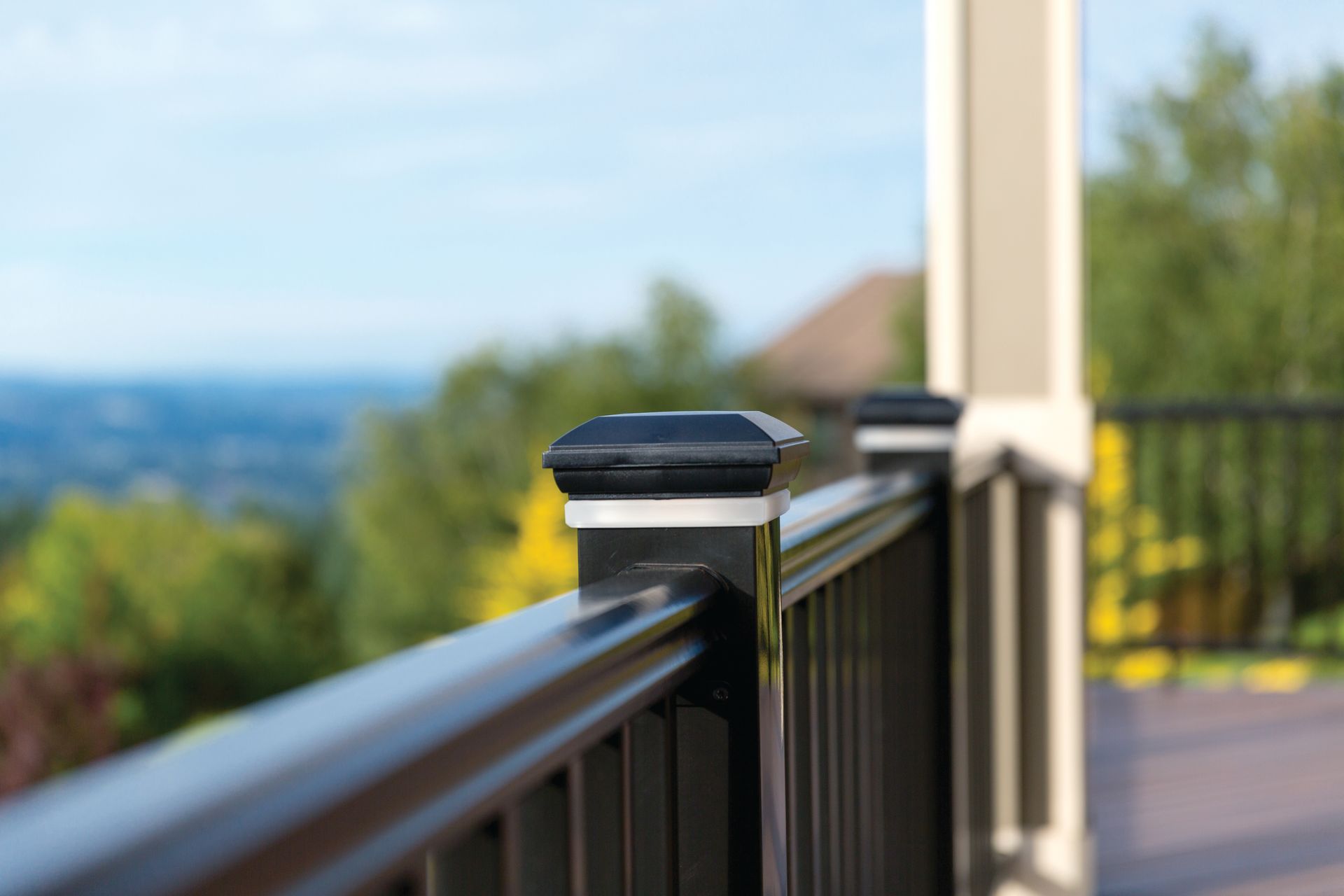 Black railing on a sunlit balcony with a blurred mountain and valley view beyond