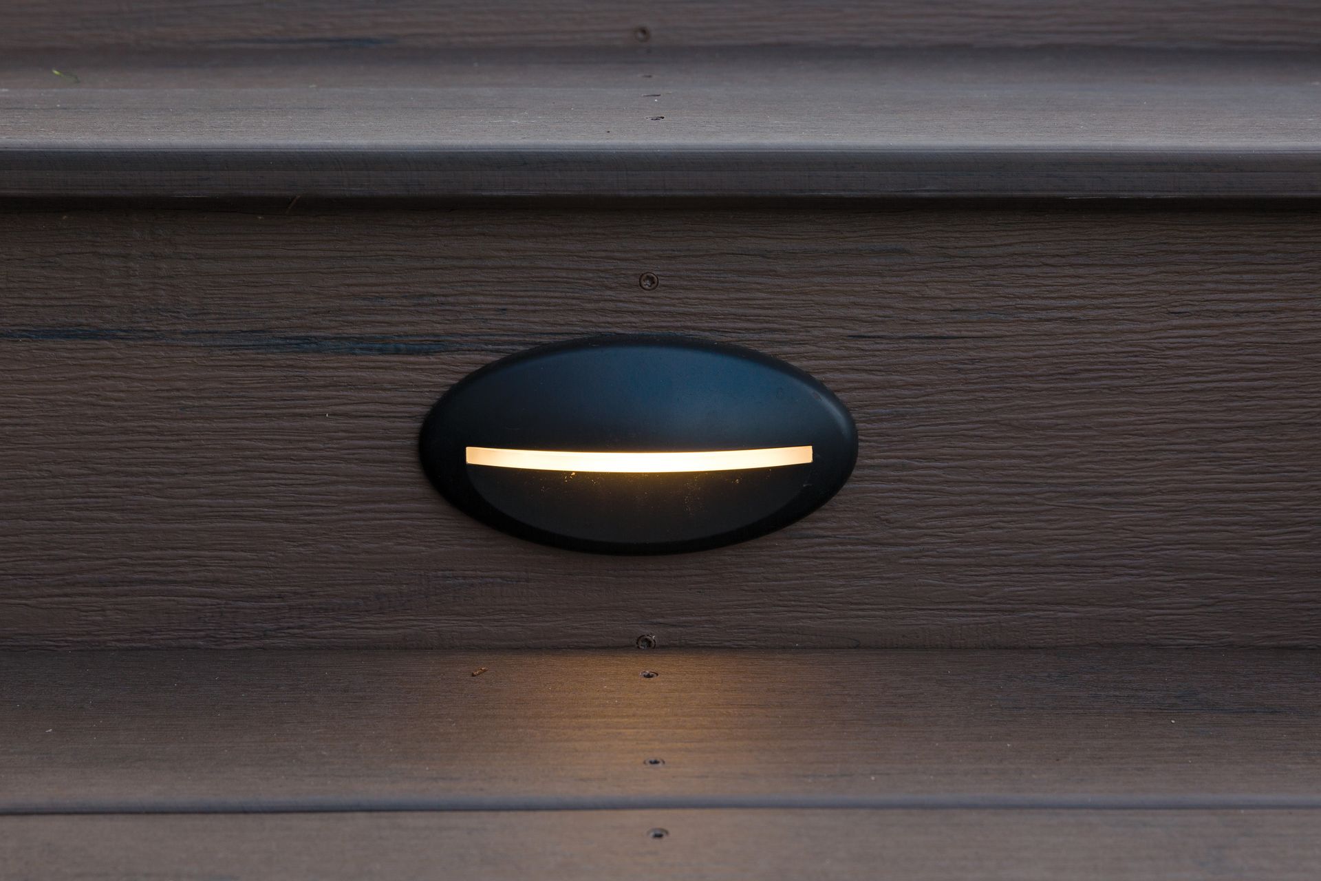 Oval black wall light glowing on a dark wooden surface