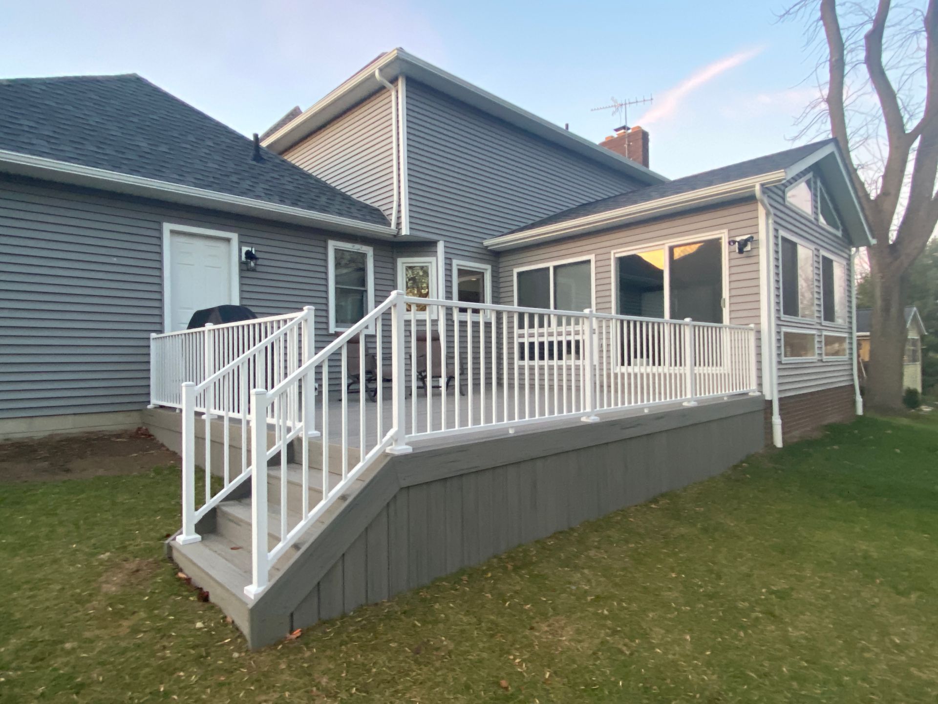 White-railed wooden deck ramp attached to a gray house in a grassy yard