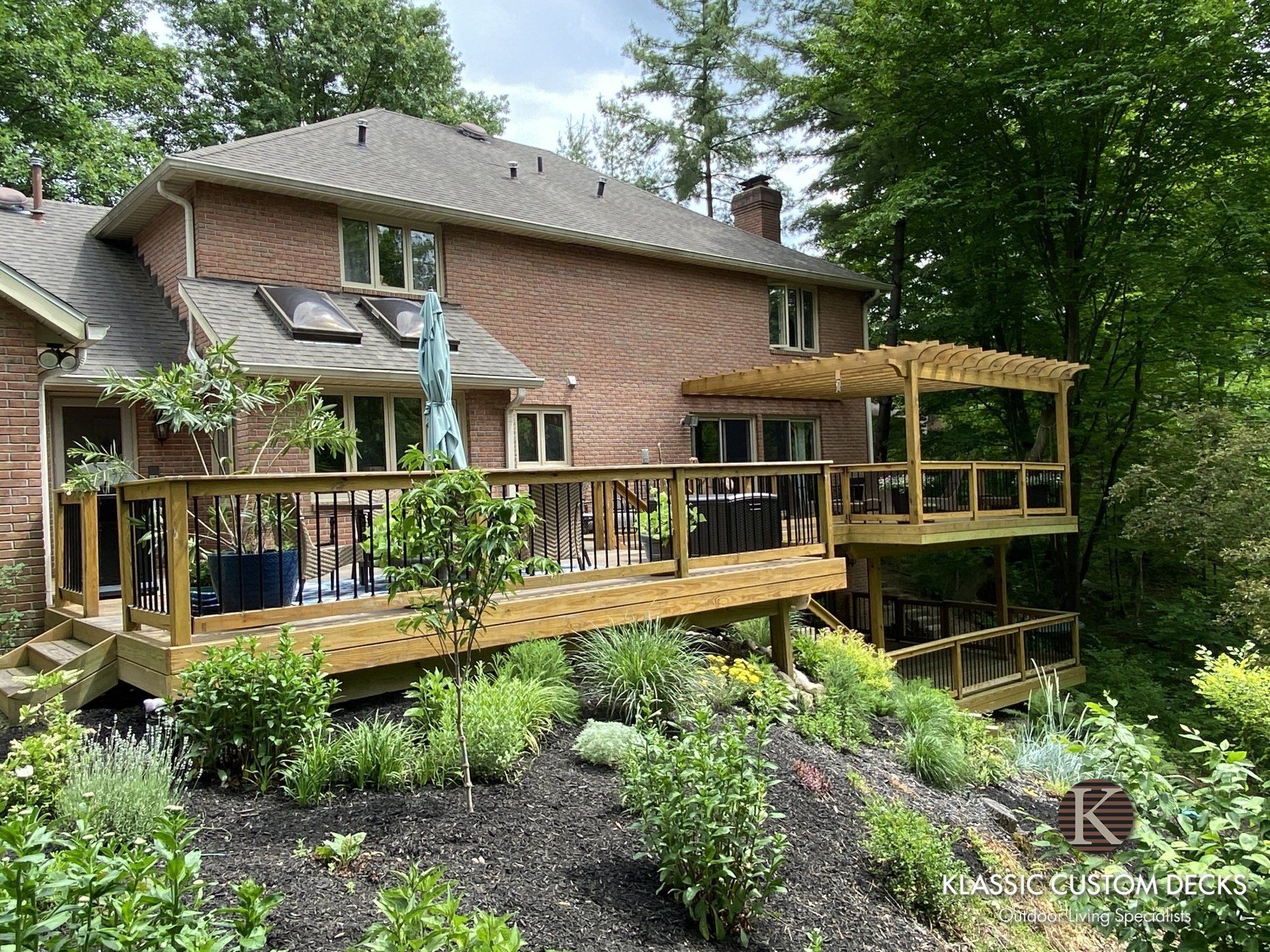 Two-story brick house with a large wooden deck overlooking a landscaped backyard and trees