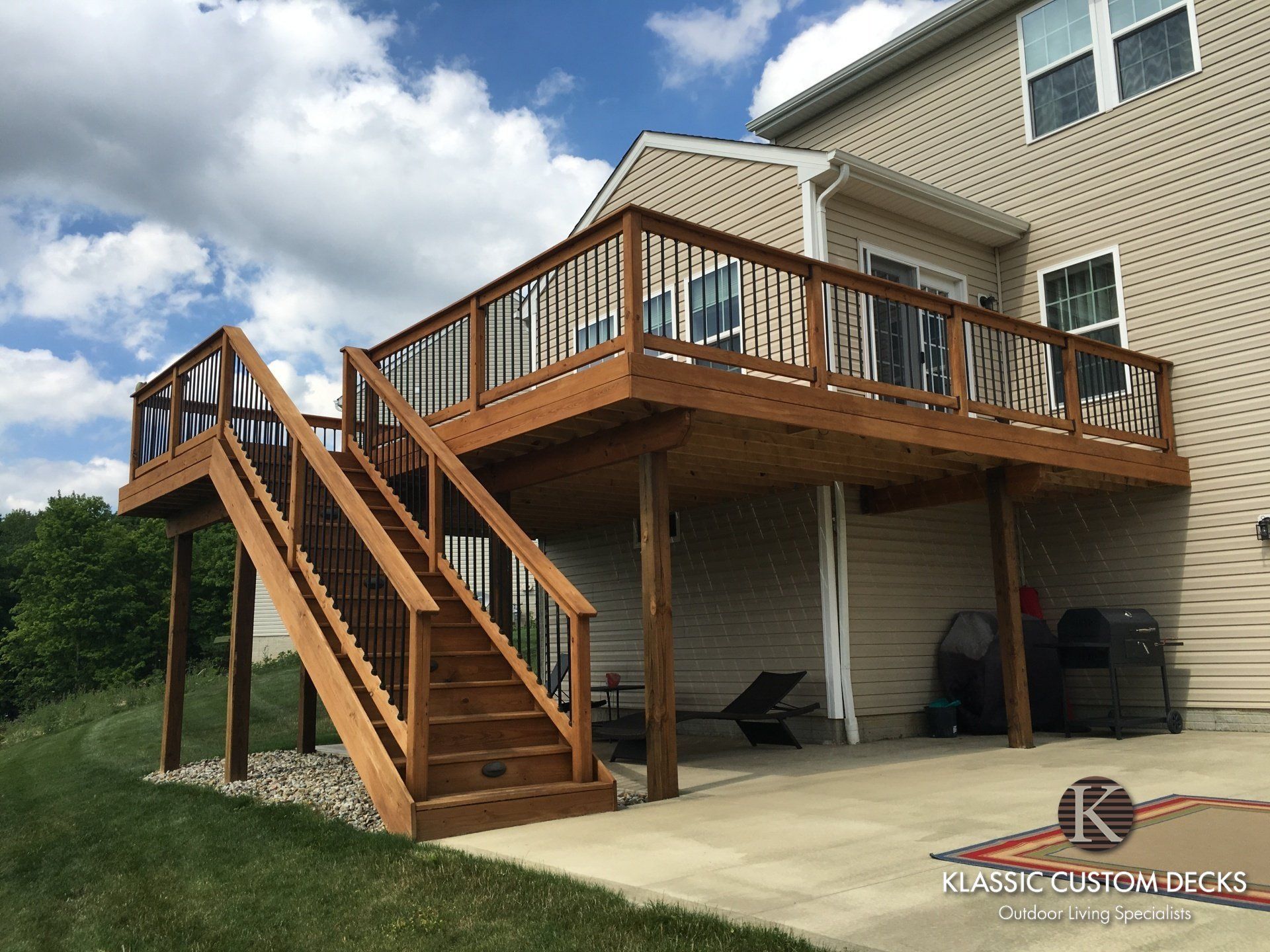 Wooden deck and stairs attached to a beige house, with a covered patio and concrete driveway underneath.