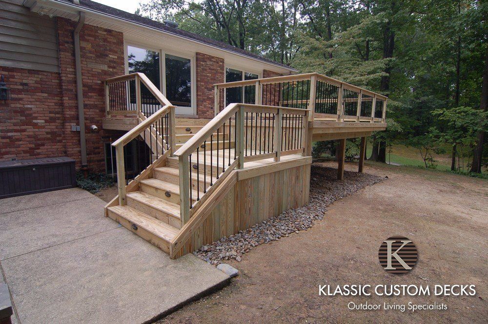 Wooden deck and stairs attached to a brick house, with ramp-style railings in a wooded yard.