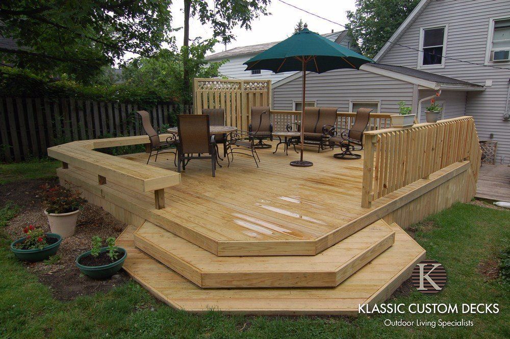 Wood deck with steps, railing, patio furniture, and green umbrella in a backyard