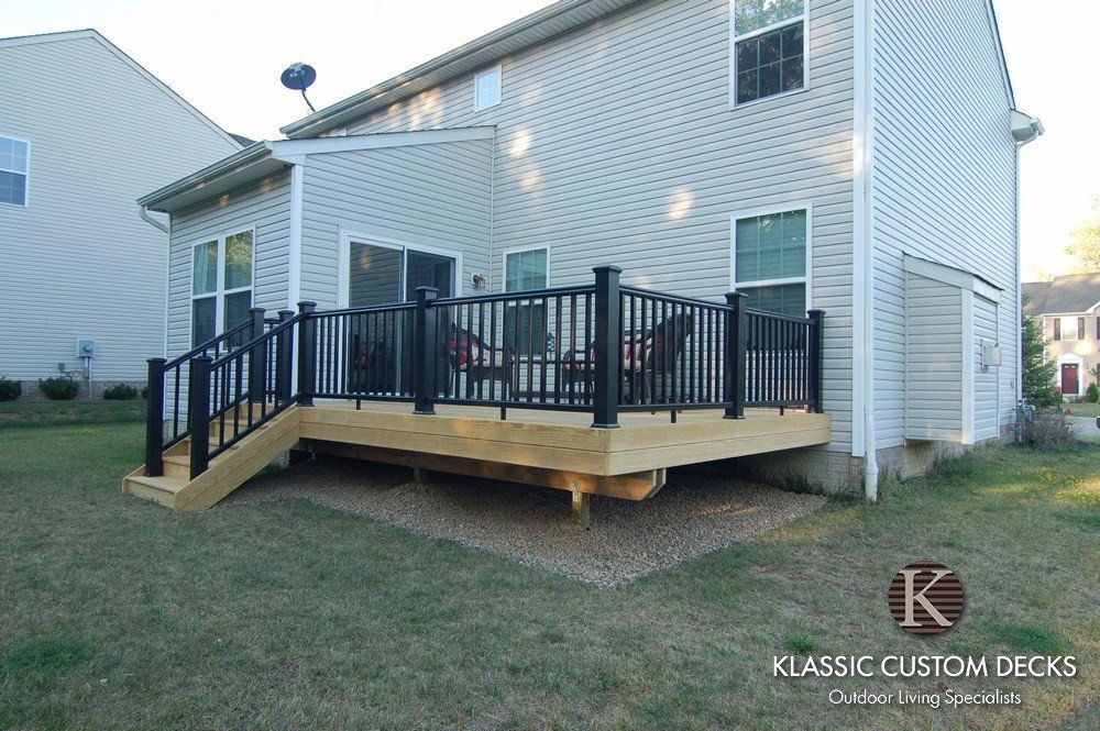Backyard wooden deck with black railings attached to a white house, viewed from the lawn