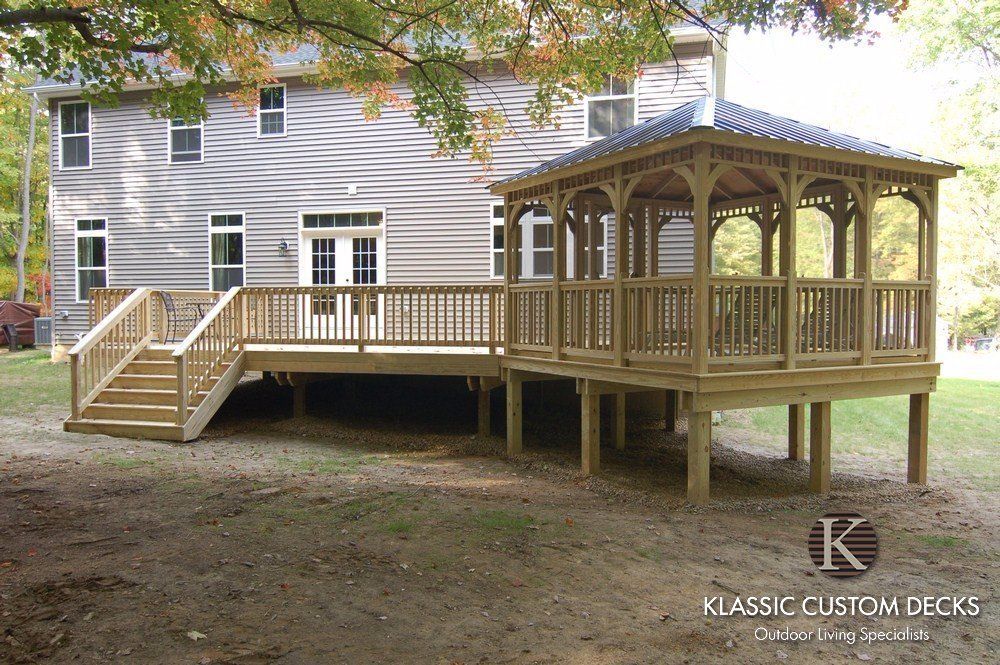 Wooden deck and gazebo attached to a gray house in a grassy backyard