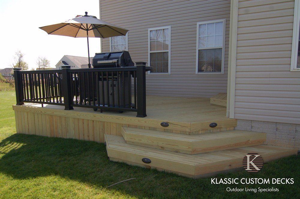 Raised wooden deck with black railing, umbrella, grill, and steps leading to a backyard lawn