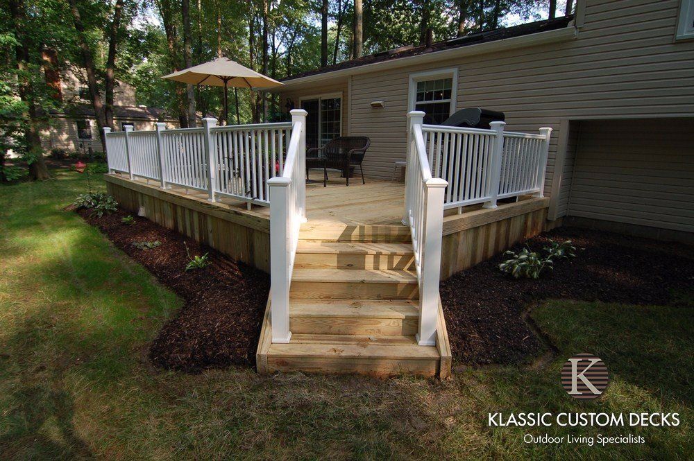 Backyard wooden deck with white railings and central steps leading to a patio and umbrella seating area