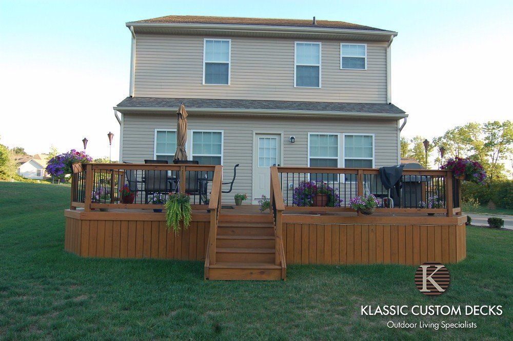 Two-story beige house with a large wooden deck and central stairs in a grassy yard.