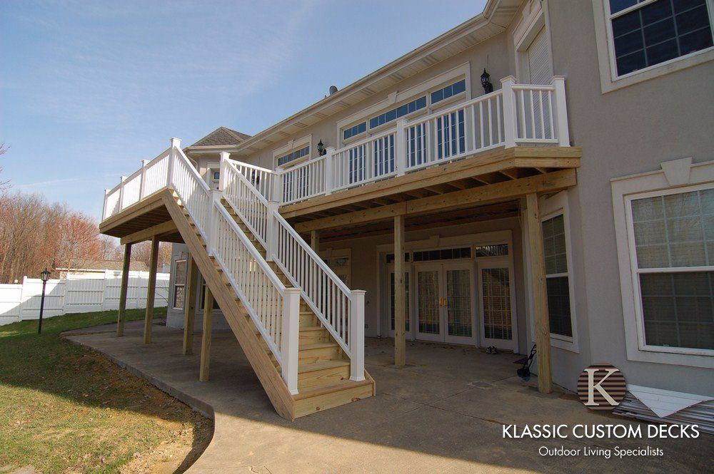 Two-story house with a raised wooden deck and stairs, white railings, and patio doors underneath