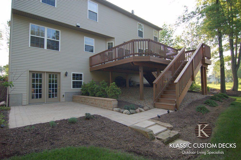 Backyard deck with curved railing and stairs on a beige house, surrounded by landscaping