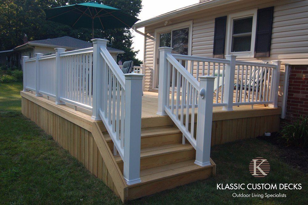 White wooden deck with stairs and railings attached to a house on a grassy yard