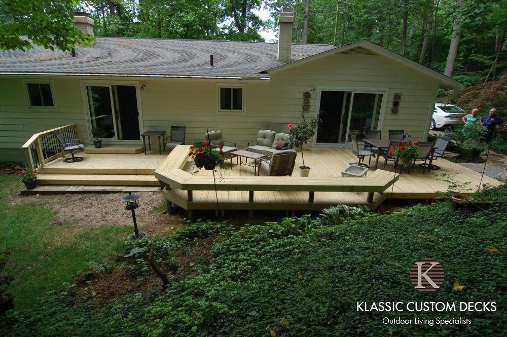 Large wooden deck with patio furniture and built-in planters beside a beige house in a wooded yard
