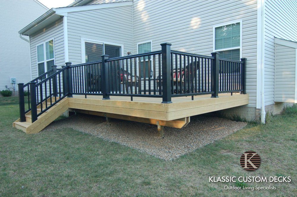 Backyard deck with black railings and wooden steps attached to a house