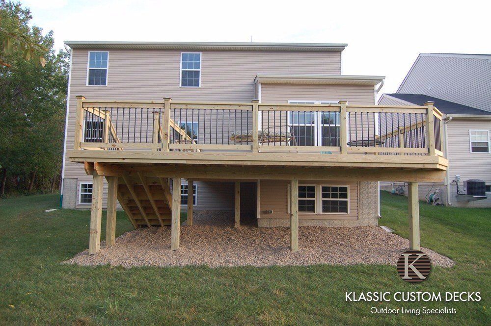 Backyard two-story house with a large elevated wooden deck and stairs above the patio area