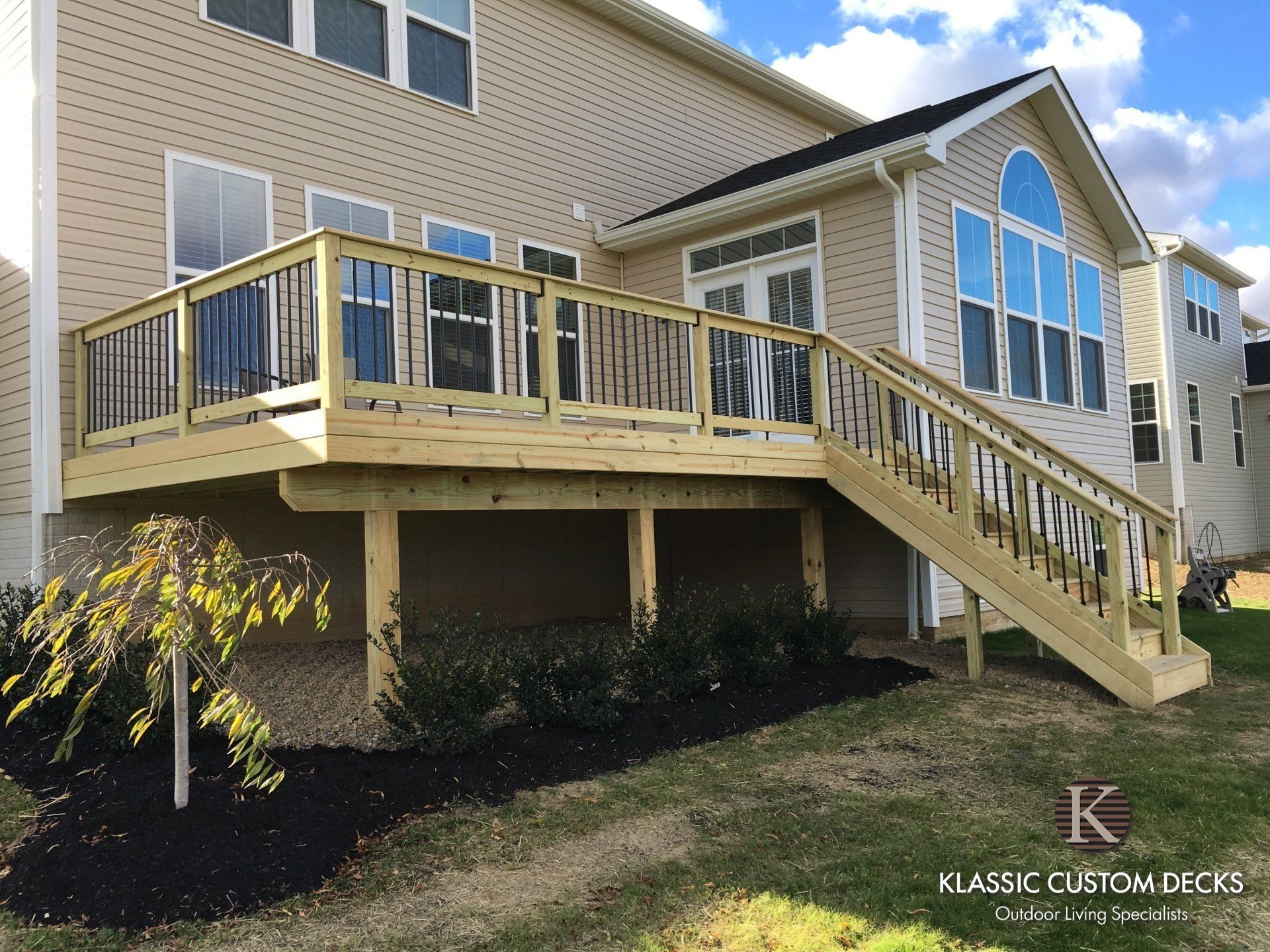 Elevated wooden deck with railing and stairs attached to a beige house with large windows