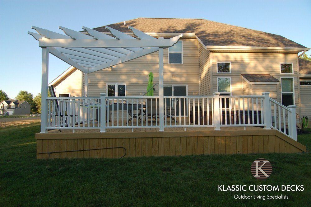 Back deck with white railings and pergola attached to a tan two-story house at dusk
