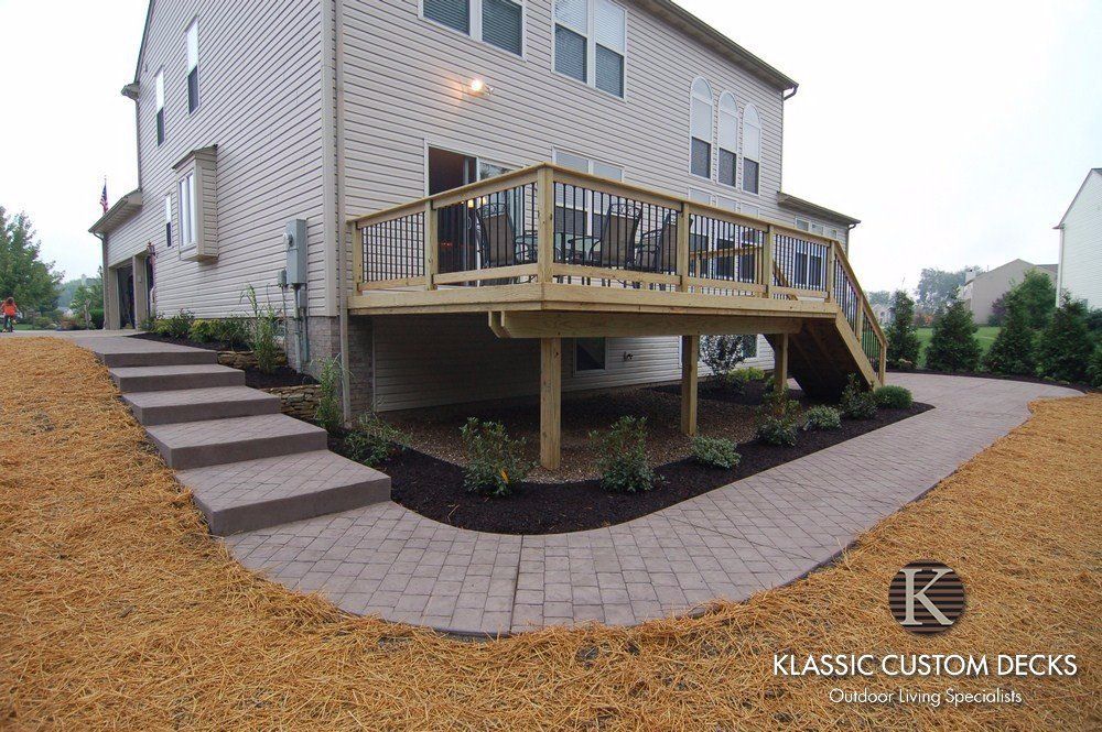 Backyard deck with stairs beside a house, featuring wood railings and brick paver patio.