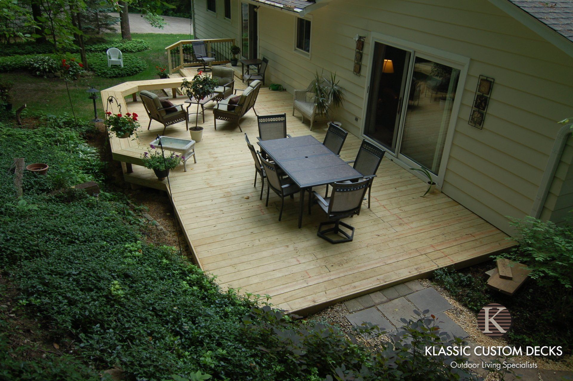 Backyard patio with outdoor dining table, lounge chairs, and potted plants beside a house.