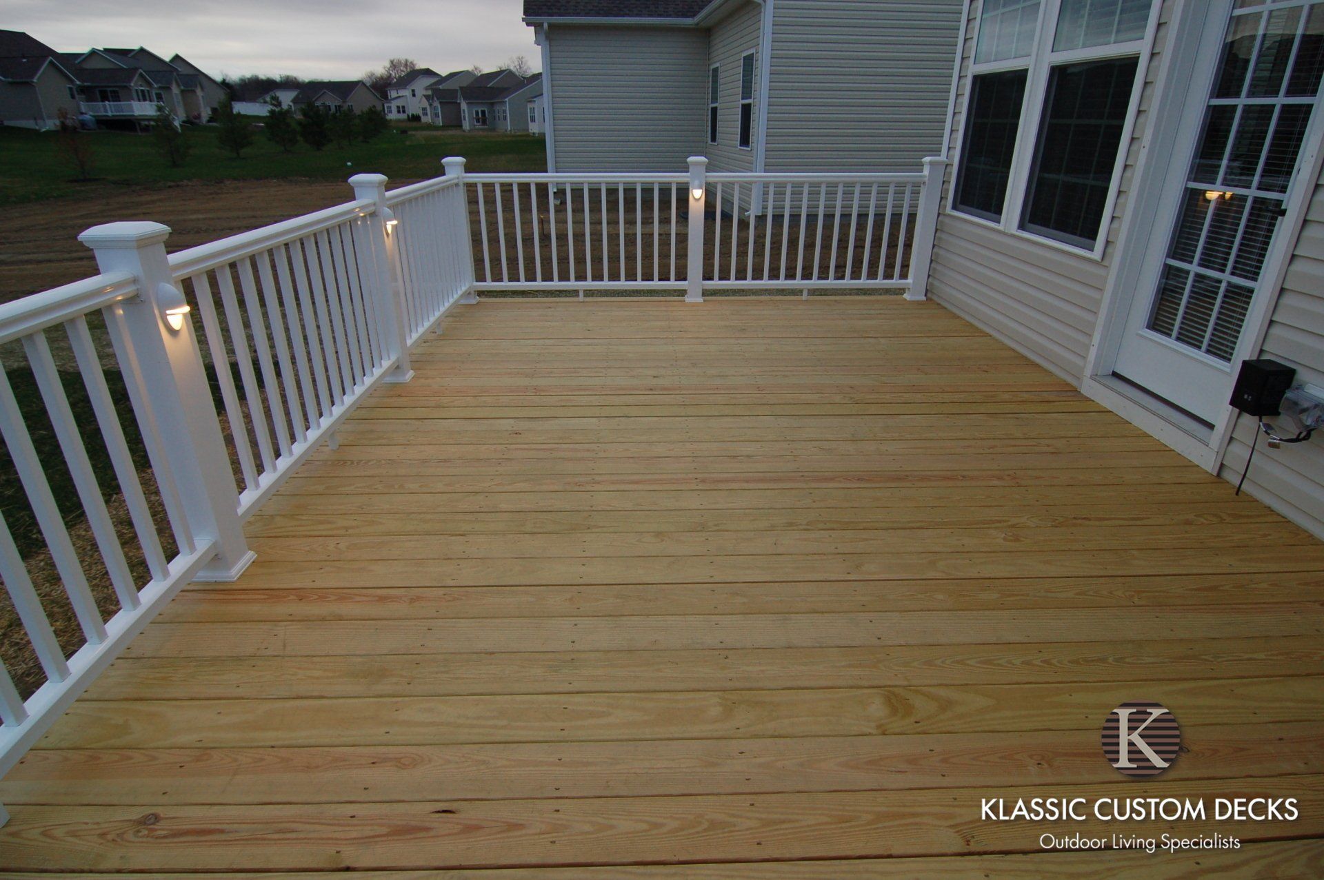 Wooden deck with white railings beside a house at dusk