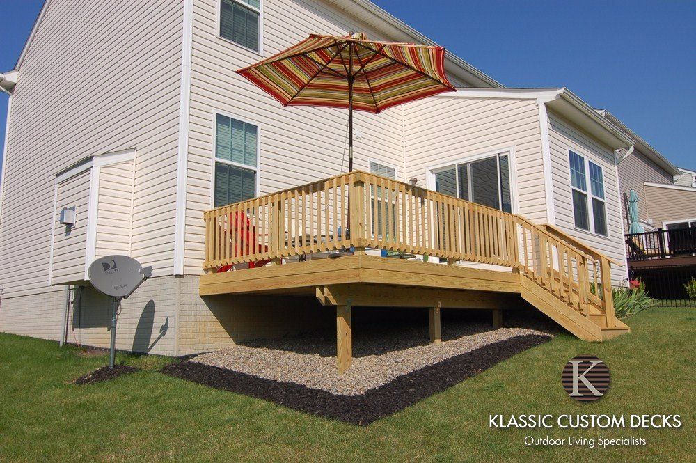Wooden backyard deck with railing and red patio umbrella beside a house