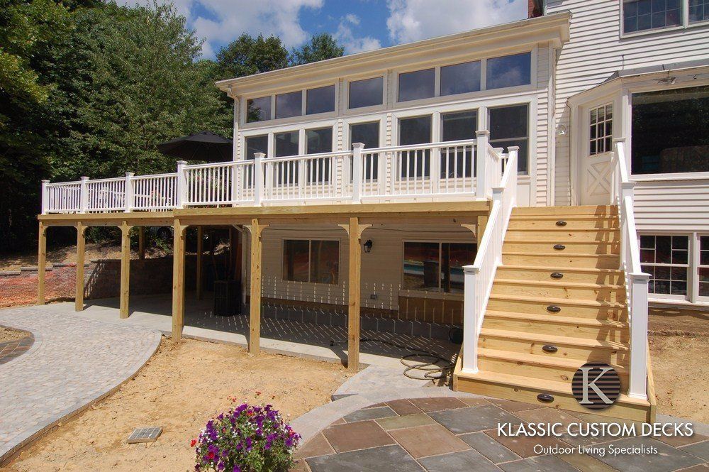 Modern white deck and elevated porch with stairs on a house, featuring wood railings and a lower patio area