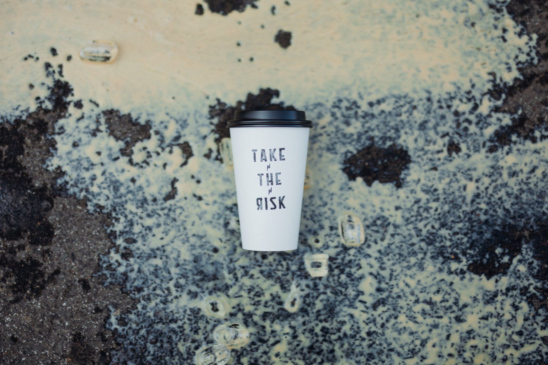 Coffee cup on a speckled surface with the words “Take the Risk” printed on it.