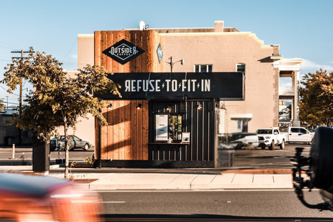Refuse to Fite storefront with black sign on a sunlit street, cars blurred in the foreground